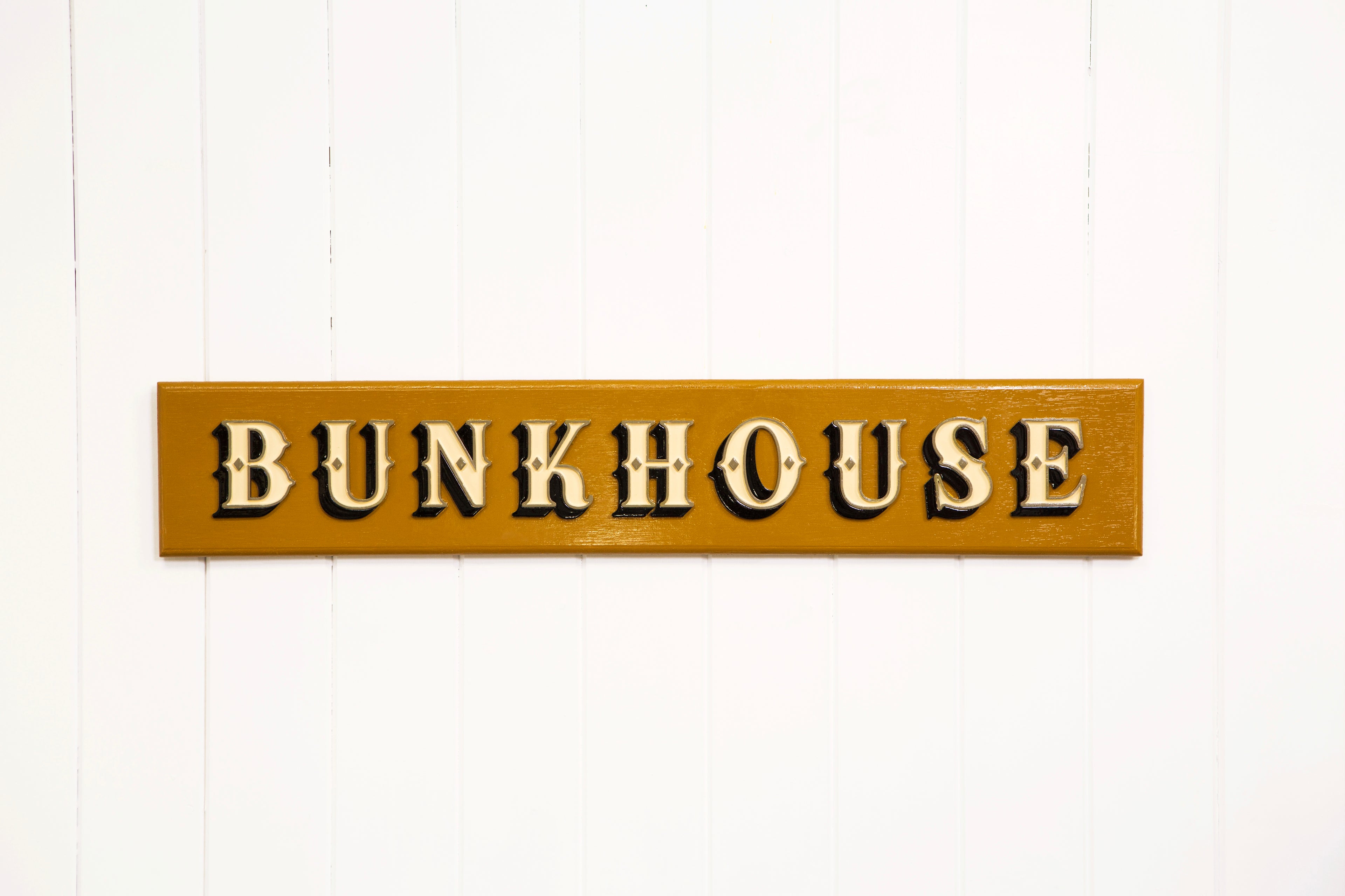 A wooden home decor sign with 3D relief lettering, spelling out the word &